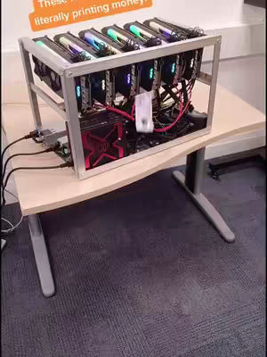 The image shows a cryptocurrency mining rig set up on a light-colored desk. The rig consists of several graphics cards mounted in a metal frame. Text overlay at the left that reads, These things are literally printing money. The background includes more office or tech room elements