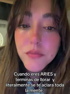 A selfie-style shot showing a woman from the chest up. She's crying, with tears visible on her cheeks and around her eyes. Her eyes are looking down. The text overlay at the bottom provides context, linking her expression to the Aries zodiac sign.