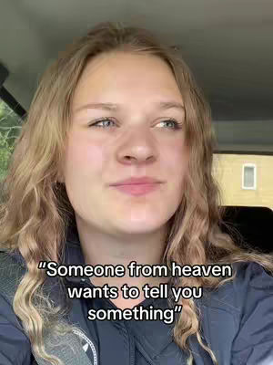 A young woman with blonde, wavy hair is visible from the chest up, framed against what appears to be the interior of a car. The background is slightly blurred, suggesting movement or a shallow depth of field. Overlaid text at the bottom announces, "Someone from heaven wants to tell you something."