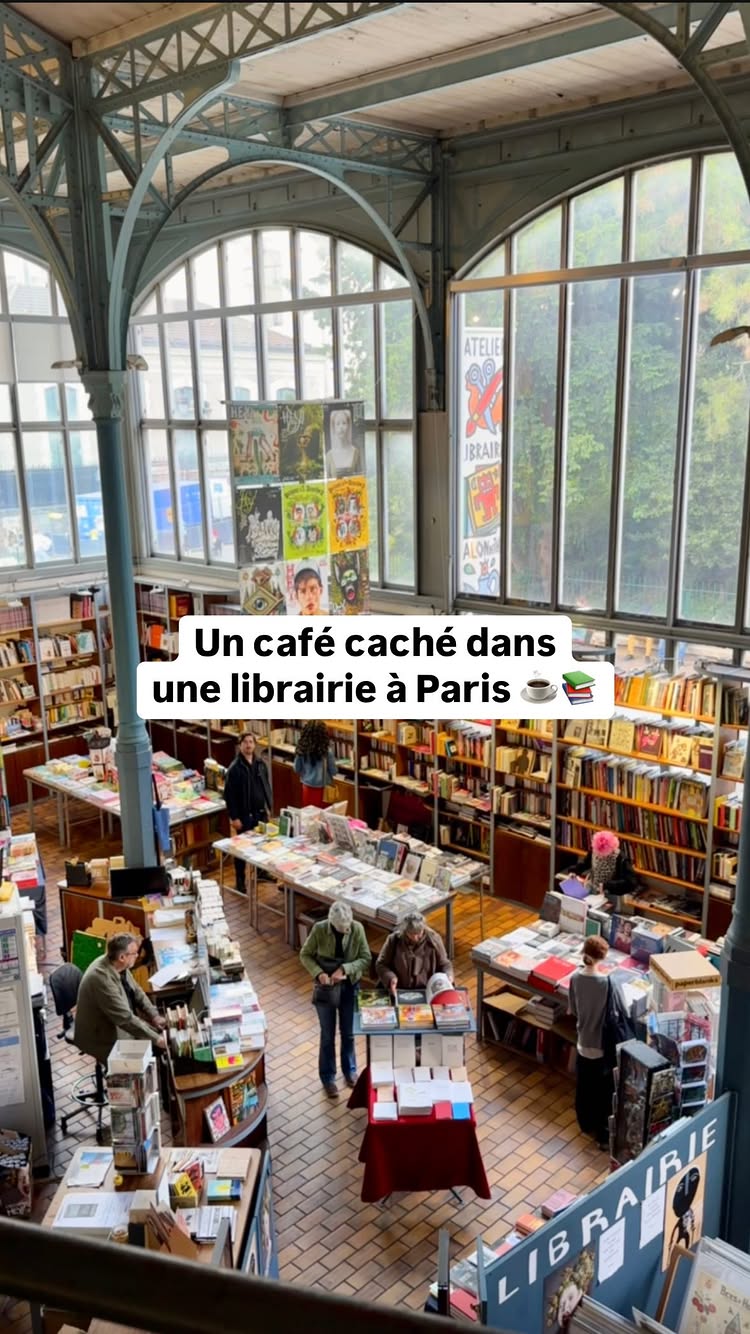 An interior shot of a cafe and bookstore. The space is open and airy with tall windows. Sunlight streams in. Bookshelves line the walls. In the foreground, there are tables with books and people browsing. The hook text is written on the bottom, left-side of the picture, which reads: Un café caché dans une librairie à Paris. The overall composition is well-lit and inviting.