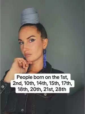 A woman with light skin and dark hair is centered in a photo with a gray background. She has a white banner over her in which text is displayed. She is gazing at the camera with her head turned slightly. Her right hand is close to her face. She has a silver head wrap. Her earrings are blue. She is wearing a black denim jacket.