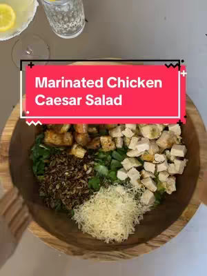 The cover image shows a top-down view of a wooden bowl filled with a Caesar salad. The salad is divided into sections: leafy greens, croutons, grated Parmesan, and marinated chicken. A glass of water and a lemon garnish are partially visible in the top left corner.