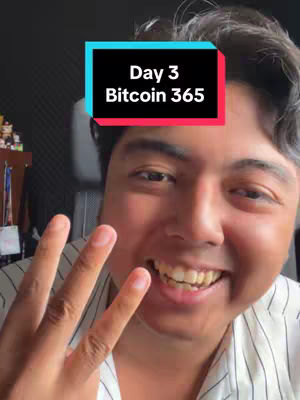 A selfie-style video cover image features a smiling man. He is holding up three fingers. Overlayed on his forehead is a rectangular box with rounded corners, containing the text 'Day 3 Bitcoin 365'. The background suggests an indoor setting with dark walls and some items on a shelf to the left.