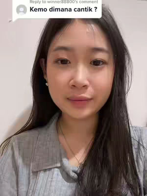 A young woman with long, dark hair and fair skin is centered in a close-up shot. She looks directly at the camera with a neutral expression. She wears a gray shirt and a delicate necklace. A comment bubble with text is in the upper left of the frame.
