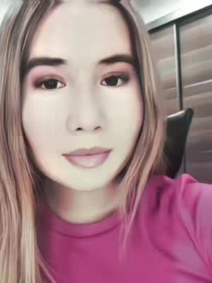 The cover image is a selfie-style shot, presenting a close-up of a person's face, framed with long, light-colored hair. The individual, with fair skin and visible eye makeup, is wearing a pink shirt. The background is slightly blurred, showing a glimpse of what appears to be a neutral-toned wall and some furniture, suggesting an indoor setting. The face's expression is neutral. The lighting appears soft and even, illuminating the face directly. The overall composition is simple and direct.