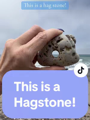 A person's hand holding a gray stone with a hole in the center. The background shows a beach with water and sky. Text overlays are present, with a TikTok logo in the corner.