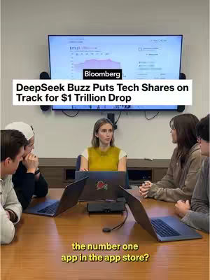 A video cover image showing a group of people seated around a table, seemingly in a business setting, with a woman in a yellow top in the center. Behind them, a television screen displays a graph from Bloomberg and white text on a black bar. Below the group, a yellow text overlay reads, 'the number one app in the app store?'