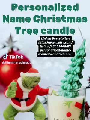 The cover image features a product shot for a personalized name candle. The main focus is on a Grinch figurine in a Santa suit, reaching towards a glass containing the candle, which looks like a tree. The background is a blurred out Christmas-themed background. A "Link in Description" call-to-action overlay directs to an Etsy listing.