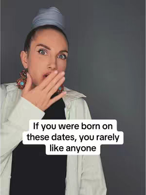 A woman with light skin is shown at the center framed from the chest up, with a hand covering her mouth and wide eyes that communicate the impact of the words displayed across the background. She's wearing large earrings, a button-down over a black shirt, and a light blue head covering. The background is a solid gray color.
