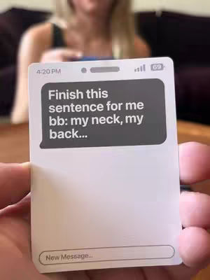A person's hand holds a phone-shaped card displaying a mock text message conversation. The background is blurred, showing a person. The text message reads, 'Finish this sentence for me bb: my neck, my back...'. The time 4:20 PM and battery '69' are shown.