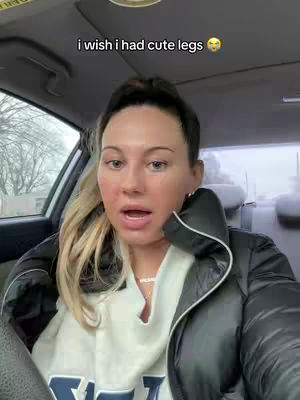 A woman is seated in a car, facing the camera. Text overlayed says, 'i wish i had cute legs' with a smiling emoji.