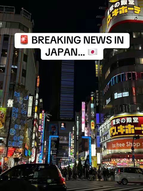 A nighttime view of a brightly lit street in Japan, showcasing numerous neon signs and buildings. A text overlay reads "BREAKING NEWS IN JAPAN". The image is a vertical shot, likely from a phone.