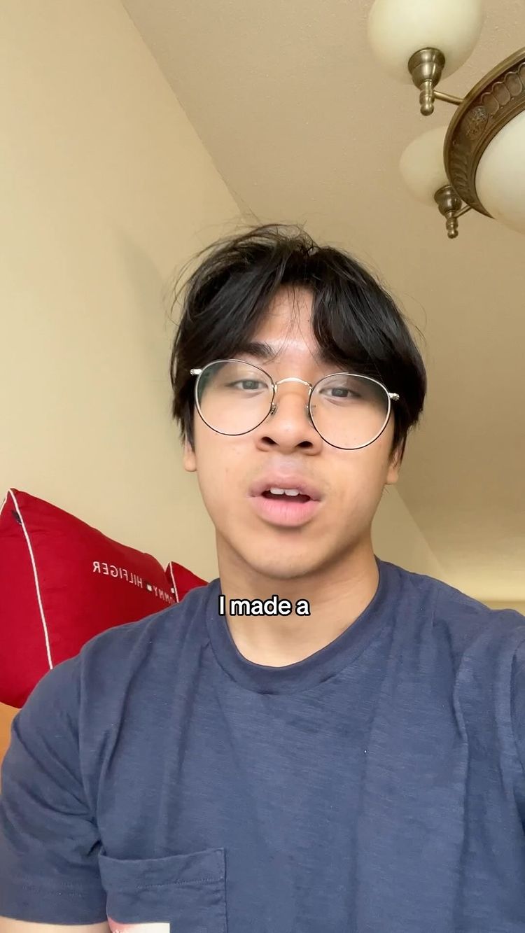 A young man with dark hair and glasses is looking at the camera indoors. Above him, parts of a ceiling fan are visible. The hook text "I made a" is added near the bottom.