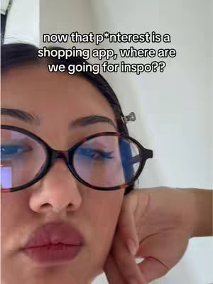 A close-up shot of a person's face wearing glasses. The person has dark hair and is gazing downward, with their hand gently touching their cheek. The background is blurred.