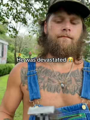 The image shows a man outdoors. He has a beard, a military-style cap, and is shirtless, wearing blue overalls. The text overlay says, \"He was devastated\" indicating a prank in the video.