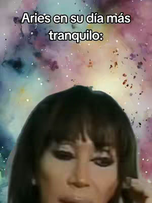 The cover image shows the close-up of a woman's face, likely a celebrity, in front of a blurred, colorful, galaxy-like background. The woman has dark hair and is facing slightly downward, with a neutral expression. Text overlayed on the image says 'Aries en su día más tranquilo:' in white font, positioned towards the top left.