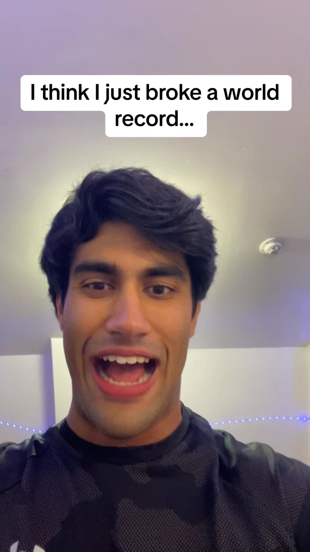 A young man with dark hair and a black t-shirt is looking at the camera with an open mouth and excited expression, a text overlay reads: 'I think I just broke a world record...'