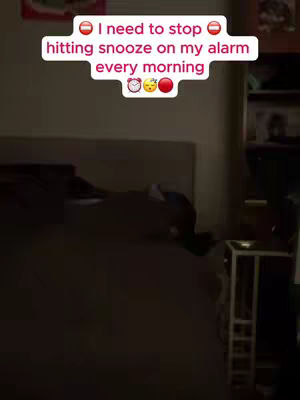 The image shows a dimly lit bedroom with a person under the covers of a bed. A text overlay is over the image, and it displays the text 'I need to stop hitting snooze on my alarm every morning'.