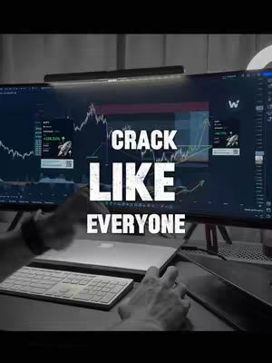 A desktop setup featuring a large monitor displaying a stock market chart, a laptop, keyboard, and a sign that says "CRACK LIKE EVERYONE" with the first two words in very big letters and the third one in a smaller font.