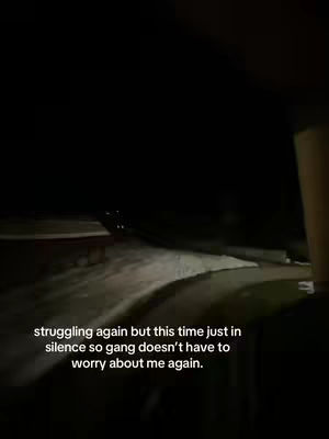 The image shows a dark, nighttime scene. A road curves into the distance, with what appears to be snow or ice on the sides. The foreground is obscured, possibly by the interior of a vehicle or a dark space. A text overlay in white letters states, “struggling again but this time just in silence so gang doesn't have to worry about me again.”