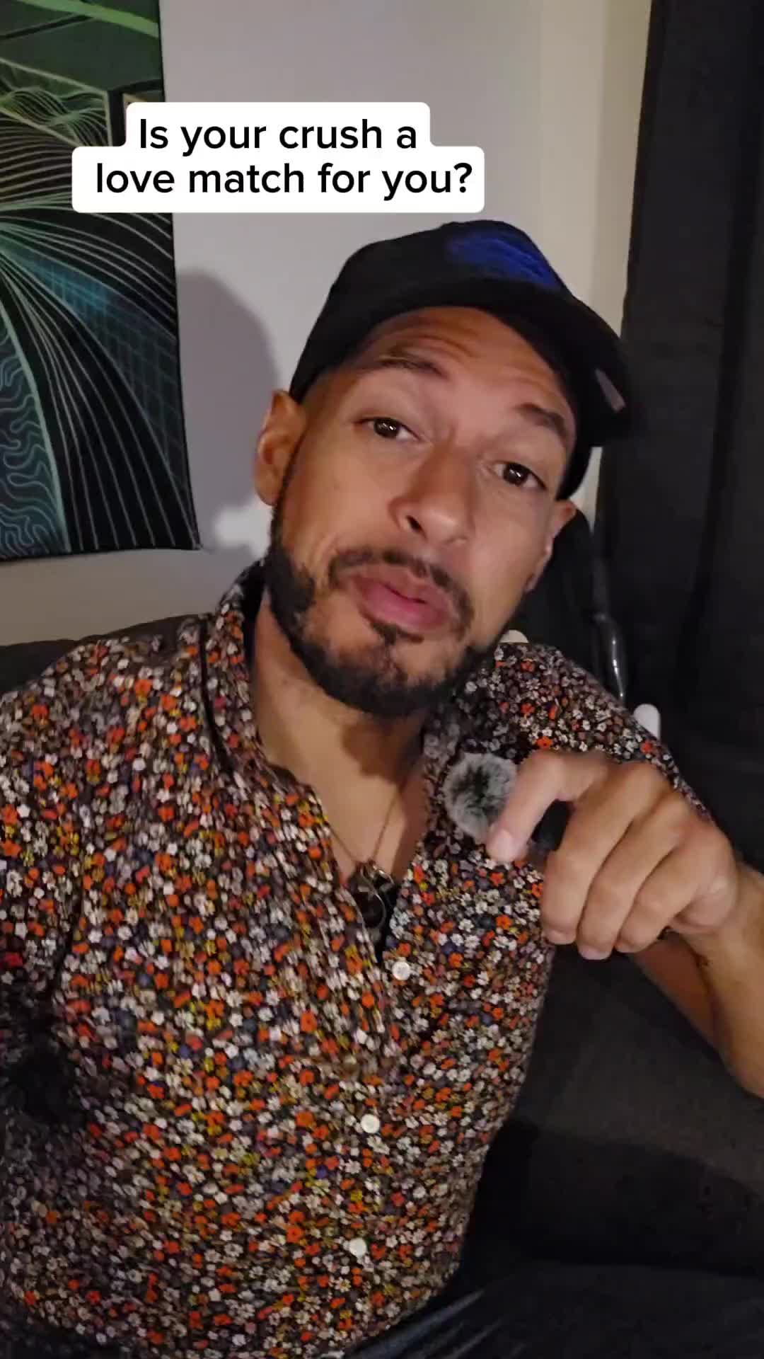 A man with a patterned shirt and a black cap is looking directly at the camera, with a microphone in his hand. A text overlay says "Is your crush a love match for you?"