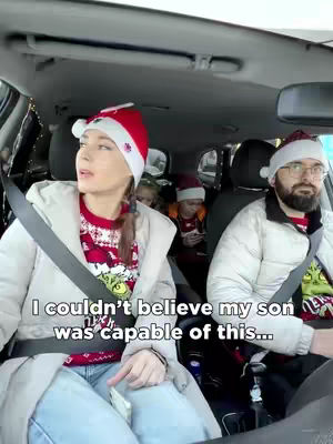 A woman wearing a Santa hat and a festive sweater is driving in a car. The image shows the woman in the front seat, with a man wearing a Santa hat driving, and two children in the back seats.