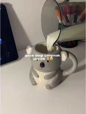 The image shows a koala-shaped mug being filled with a white liquid. The mug is gray and set on a white surface. In the background, another container possibly a pitcher, is visible. Text is overlaid on the image.