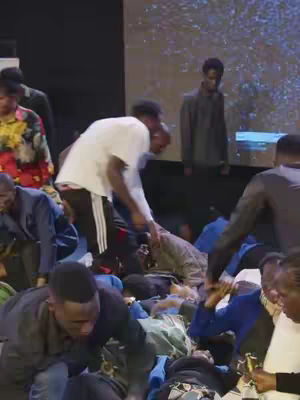 A group of people are on the floor, some appear to be lying down. There are also people standing around. The lighting is focused where the people are on the floor.