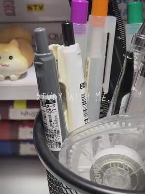An eye-level shot focused on various stationery items such as markers, pens, and a pencil cup which comprises a black mesh holder. The items are brightly colored and against a blurred background.