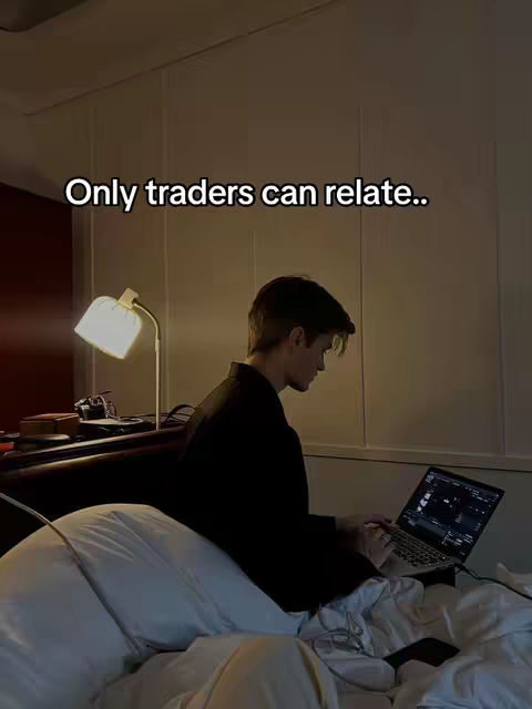 A man sits in bed with a laptop, illuminated by a desk lamp. The text overlay reads, 'Only traders can relate..'