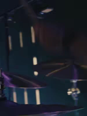 The image focuses on a musical setting with cymbal drums in the foreground and a dimly lit background suggesting a stage or studio. Vertical lines of light add depth.