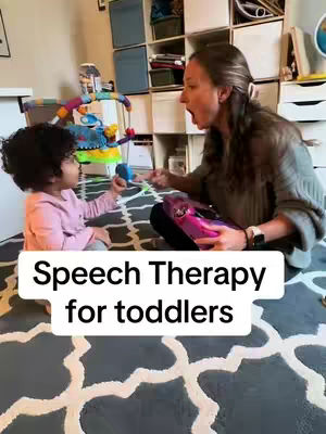 A woman and a young child are playing in front of a colorful play gym in a room. The woman is looking at the child with her mouth open, as if she is about to say something. The child is looking at the woman and holding something in their hand.