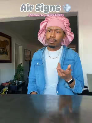 A man wearing a pink headscarf and a blue denim jacket is the central focus. The background blurs to suggest an interior space. Text overlays at the top proclaim: \"Air Signs\" and list related zodiac signs. The man is smiling and gesturing with his right hand.