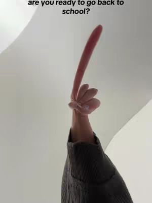 A low-angle shot looking up at a person's hand holding up a foam finger against a white background. The hand is partially visible, with a dark sleeve covering the arm. The foam finger is light pink, angled upwards. The background is plain white, suggesting a bright, possibly indoor setting. At the top, there is text that asks 'are you ready to go back to school?'