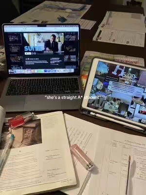 An image showing a study setup with a laptop displaying a streaming service, an iPad, notebooks, and papers scattered on a wooden table. The text overlay reads, "she's a straight A* student."