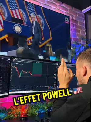 A man is sitting in front of three computer monitors displaying stock charts. A large screen behind shows a man in a suit walking on a stage, likely Jerome Powell. Text overlayed on the image reads "L'EFFET POWELL". The image has a modern aesthetic, with bright colors from the monitors and plant life, combined with a brick wall, making it a dynamic composition capturing attention.