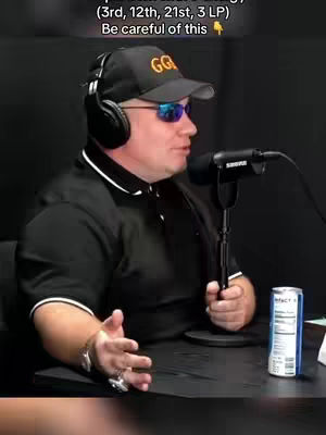 A man in a black shirt, sunglasses, and a baseball cap with a logo is speaking into a microphone. A can of soda sits on the table.