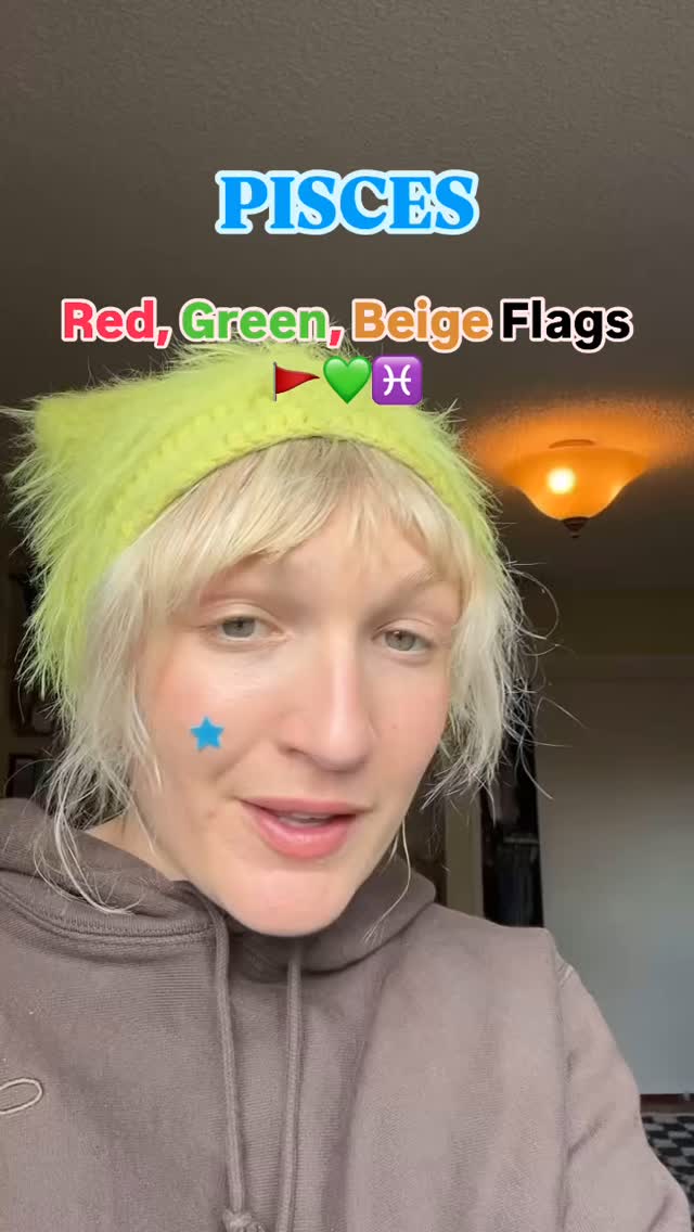 A woman with blonde hair and a bright neon green headband is the central focus, her face slightly angled towards the viewer. She has visible blush and a star-shaped sticker on her cheek. The background is a blurred interior scene with a warm-toned overhead light.