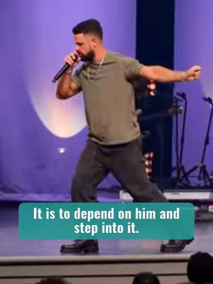 A man, presumably a preacher, is on a stage with a microphone, mid-action to deliver a sermon. He is wearing a green shirt and black pants. A teal banner adds a slogan.