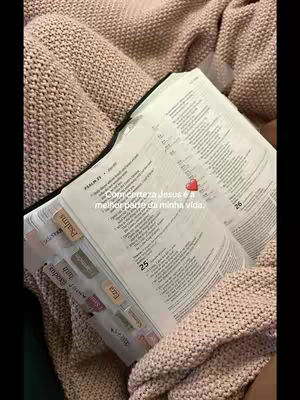 The photo shows an open book, likely a Bible, resting on a person's lap, covered by a pink knitted blanket. Text is overlaid, and the image is composed in warm, soft tones.