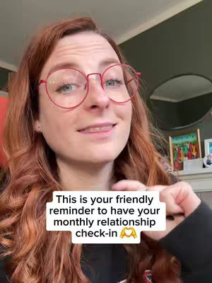 A woman with red hair and glasses smiles into the camera. A text overlay provides a reminder about a monthly relationship check-in.