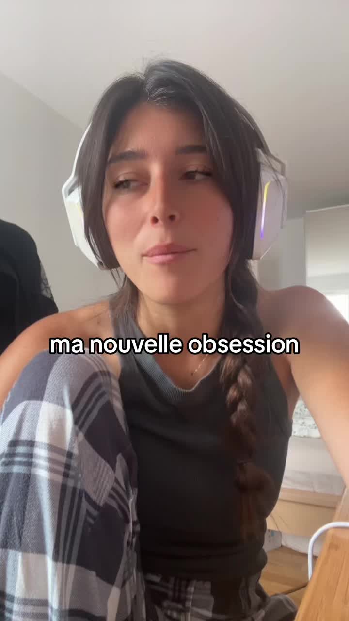The image shows a young woman with long dark hair and a braid wearing white headphones. She's in a casual setting, likely indoors, wearing a dark gray tank top and plaid pajama pants. A text overlay reads 'ma nouvelle obsession'.