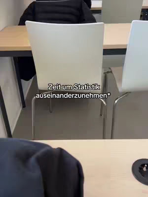 A shot from a classroom setting. A white chair is the focal point, with a table in front and another chair visible to the right. The lighting appears neutral, and the background is blurred, suggesting depth. The chair is centrally positioned and the text overlay is added.