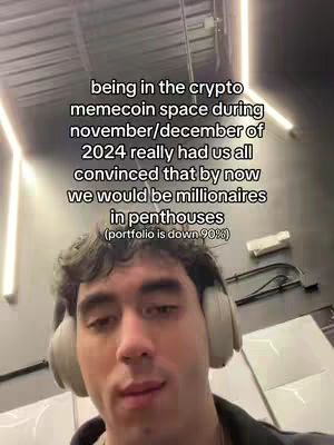 A selfie-style video with a young man wearing headphones, set indoors with overhead lighting. The man is the primary focus, with text overlaid describing the meme-coin market of November/December 2024. The background is simple with a grey-white color palette.