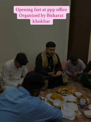 A photo taken indoors shows a group of men, some wearing religious attire, seated on the floor around plates of food. A text overlay in a pink box at the top of the image reads, 'Opening fast at ppp office Organized by Bisharat khokhar'. The group appears to be breaking fast together.