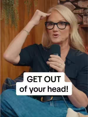 A woman with blonde hair and glasses is holding a microphone and touching her forehead, likely talking. A text overlay in a white box that says 'GET OUT of your head!' is at the bottom of the frame.
