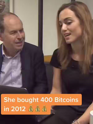 The cover image shows two people, a man and a woman, in what looks like an interview setting. The woman is on the right and is the focus of the image, speaking and gesturing slightly. The man is on the left, partially obscured by a laptop. An orange banner is overlaid at the bottom, displaying text that states, "She bought 400 Bitcoins in 2012", along with money bag emojis.