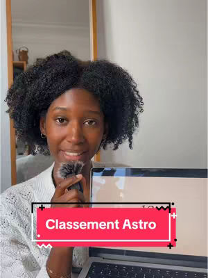 A woman with dark, curly hair and a white top smiles, holding a microphone and a laptop, with a red and white text overlay that reads "Classement Astro."