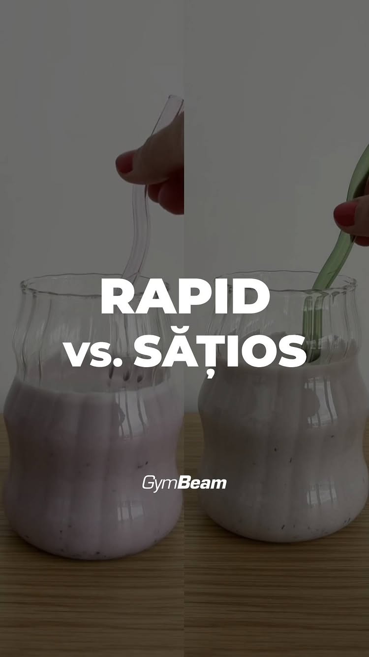 The image is split vertically, showing two servings of a pinkish, thick liquid in curvy glass cups. A hand is stirring each drink with a different colored spoon. The text overlay reads 'RAPID vs. SĂȚIOS'. The GymBeam logo is at the bottom. The background is a plain, light color.