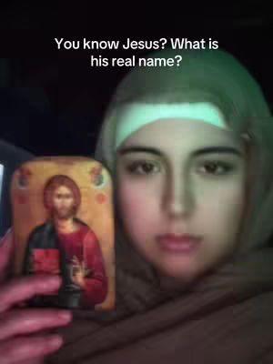 A woman holds a framed image of Jesus and looks directly at the camera. The background is dark, and the lighting appears to be from an artificial source. There is overlaid text at the top.